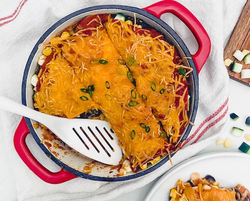 Enchilada lasagna in a Dutch oven with spatula.