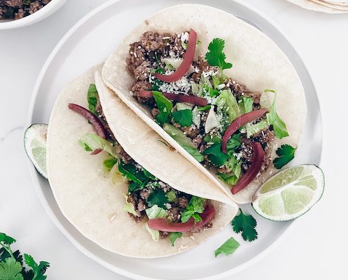 Two ground pork tacos on a white plate with cilantro and lime.