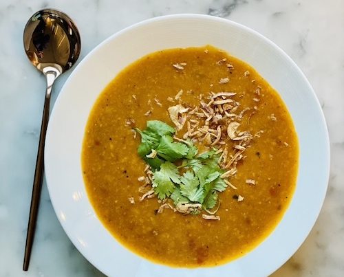 A gold spoon next to a white bowl of Indian yellow pea soup.