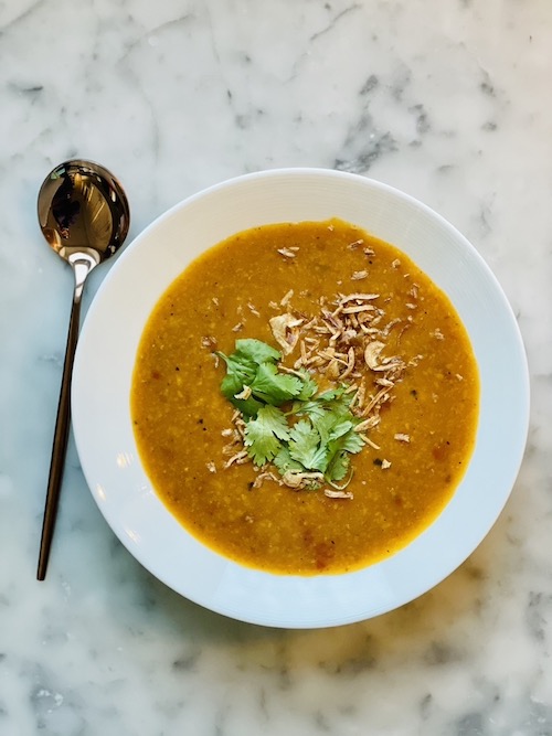 A gold spoon next to a white bowl of Indian yellow pea soup.