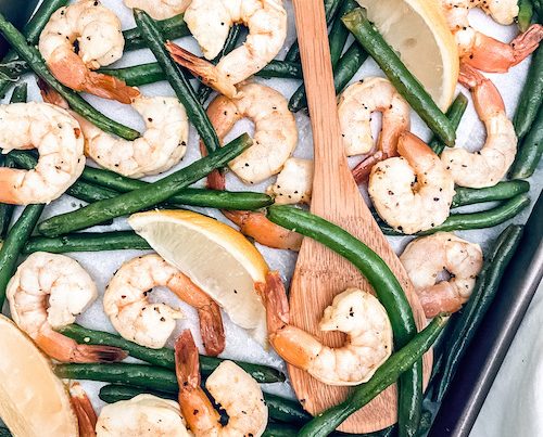 A sheet pan of shrimp and green beans accented with lemon wedges.