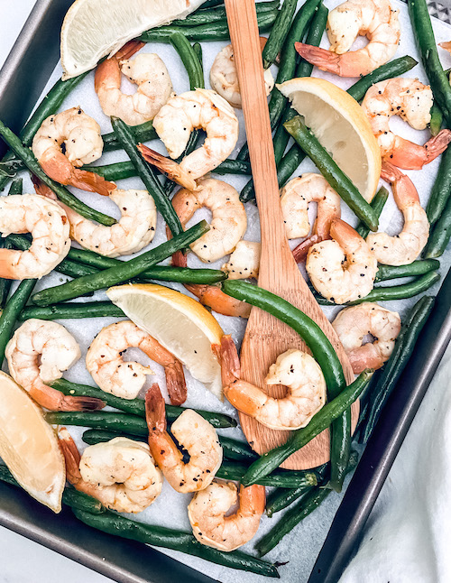 A sheet pan of shrimp and green beans accented with lemon wedges.