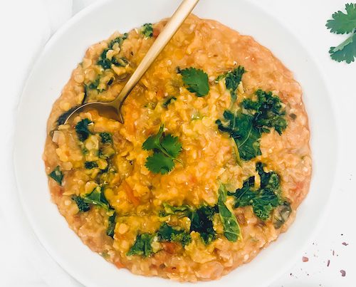 Red Lentil + Kale Daal in a white bowl with gold serving spoon.