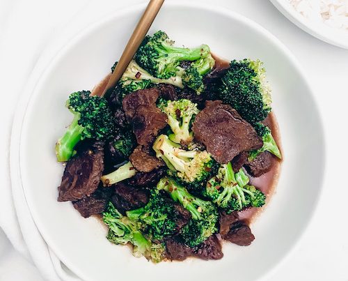 Broccoli beef in a white bowl with a golden fork.