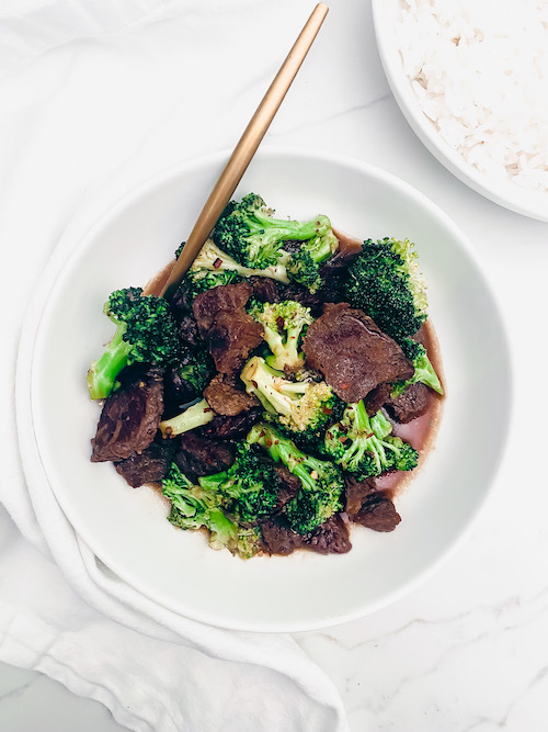 Broccoli beef in a white bowl with a golden fork.