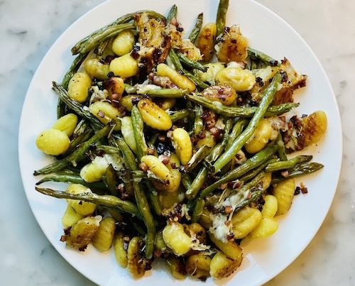 Crispy gnocchi and green beans on a white plate.
