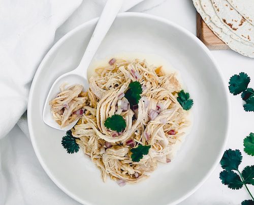 A white serving spoon in a bowl of pulled pineapple chicken.