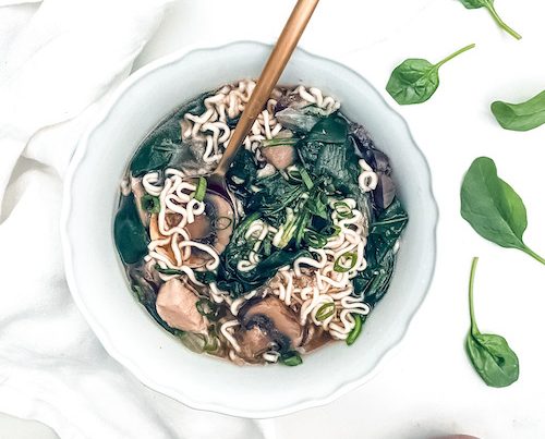 A golden spoon in a bowl of Asian-style chicken noodle soup.