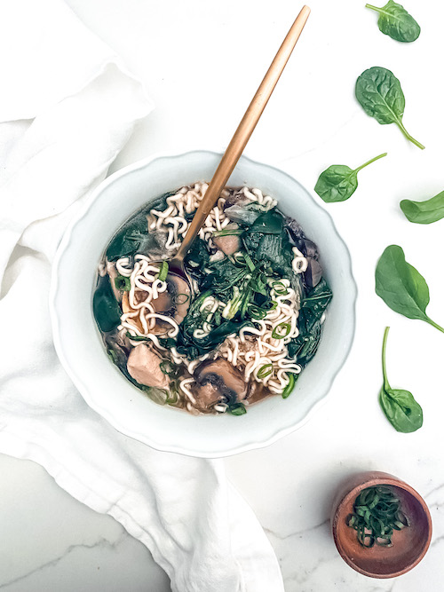 A golden spoon in a bowl of Asian-style chicken noodle soup.