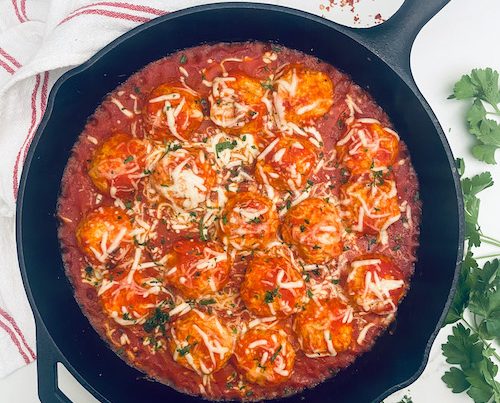 A cast iron skillet filled with cheesy chicken meatballs.