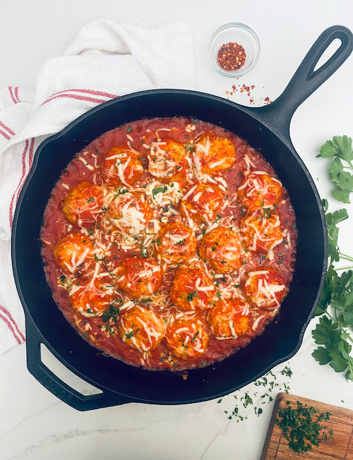 A cast iron skillet filled with cheesy chicken meatballs.