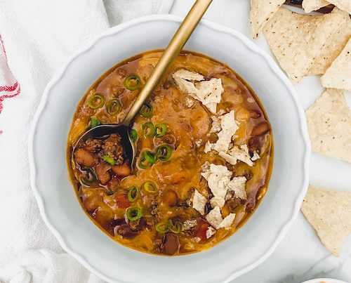 Cheese chili with tortilla chips in a white bowl.