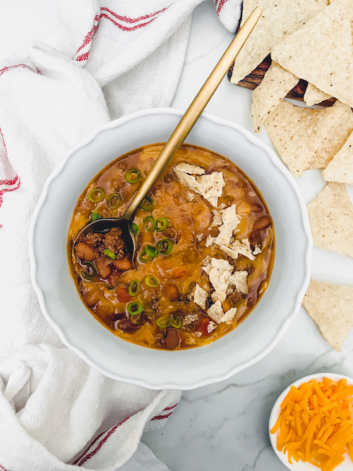 Cheese chili with tortilla chips in a white bowl.