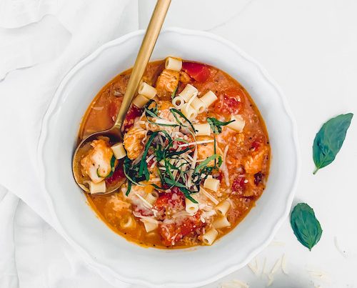 Chicken parmesan soup with a gold spoon in a white bowl.