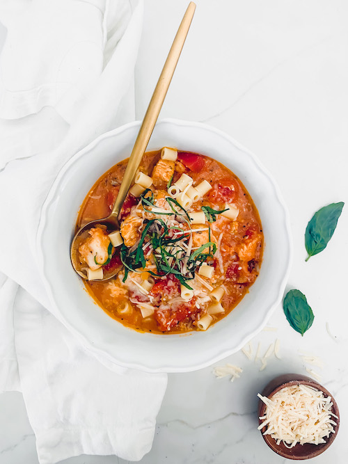 Chicken parmesan soup with a gold spoon in a white bowl.