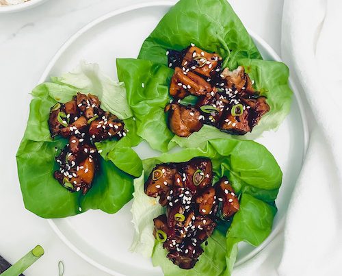Honey sesame chicken topped with sesame seeds in lettuce cups.