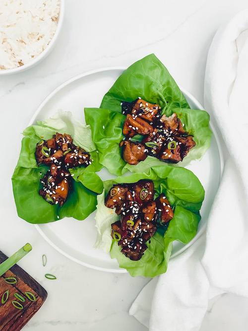 Honey sesame chicken topped with sesame seeds in lettuce cups.
