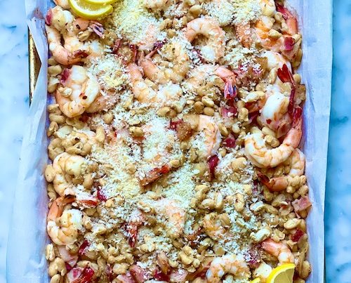 A baking sheet lined with parchment and filled with shrimp and beans.