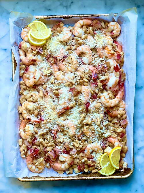 A baking sheet lined with parchment and filled with shrimp and beans.