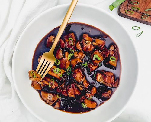 Chicken pieces in a teriyaki sauce in a white bowl.