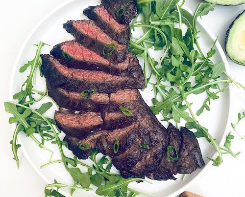Sliced skirt steak and arugula on a white dinner plate.