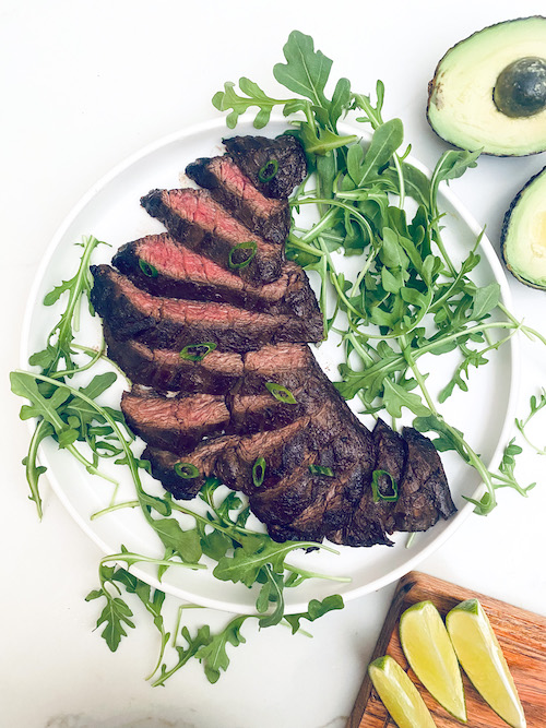Sliced skirt steak and arugula on a white dinner plate.