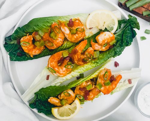 Buffalo shrimp and lime on romaine leaves on a white plate.