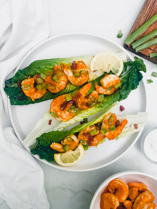 Buffalo shrimp and lime on romaine leaves on a white plate.