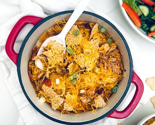 Chicken enchilada casserole topped with tortilla chips and cheese in a Dutch oven.