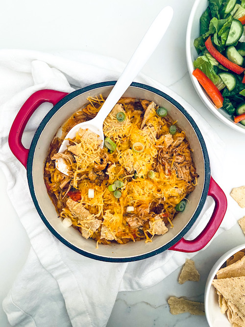 Chicken enchilada casserole topped with tortilla chips and cheese in a Dutch oven.