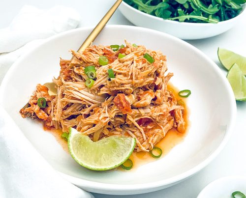Shredded salsa chicken on a white plate with a lime wedge.