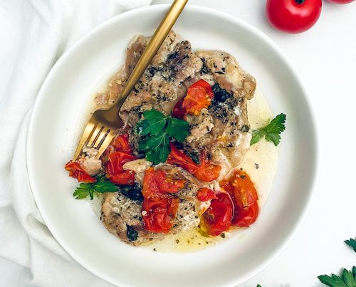 Diced chicken thighs with tomatoes in a shallow white bowl.