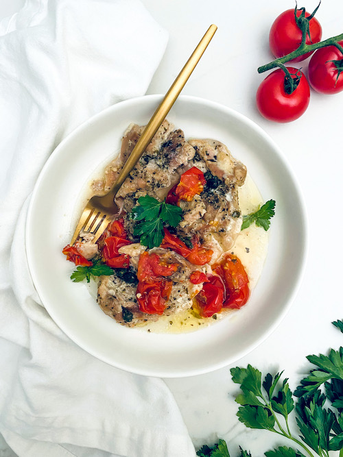 Diced chicken thighs with tomatoes in a shallow white bowl.