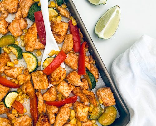 Cubed chicken and summer veggies on a parchment lined sheet pan.