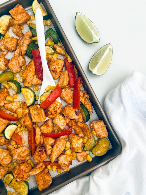 Cubed chicken and summer veggies on a parchment lined sheet pan.