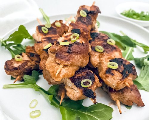 Thai chicken skewers with lettuce on a white plate.