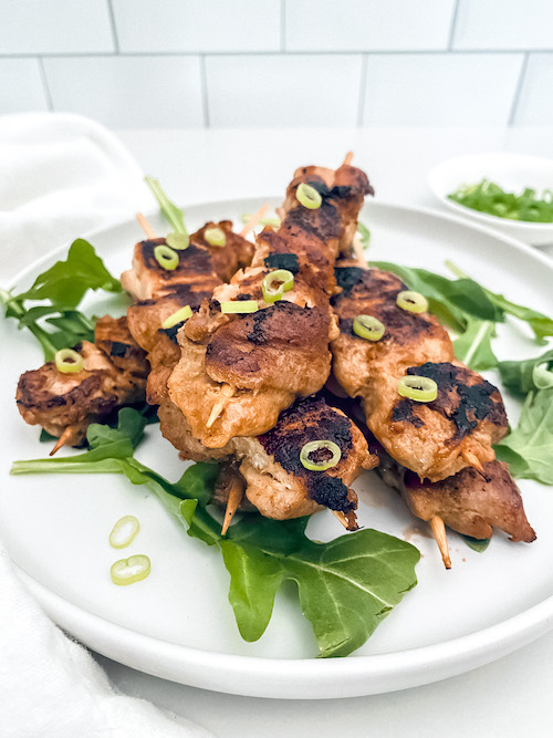 Thai chicken skewers with lettuce on a white plate.