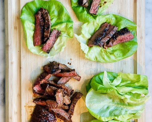 Sliced Korean-inspired steak on green lettuce leaves on a wooden cutting board.