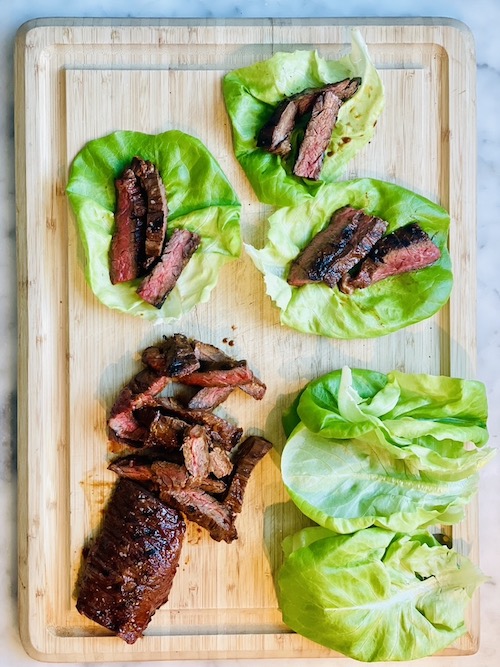Sliced Korean-inspired steak on green lettuce leaves on a wooden cutting board.