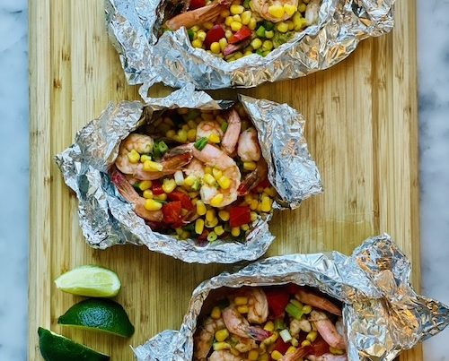 Shrimp and corn foil packets on a wooden cutting board.