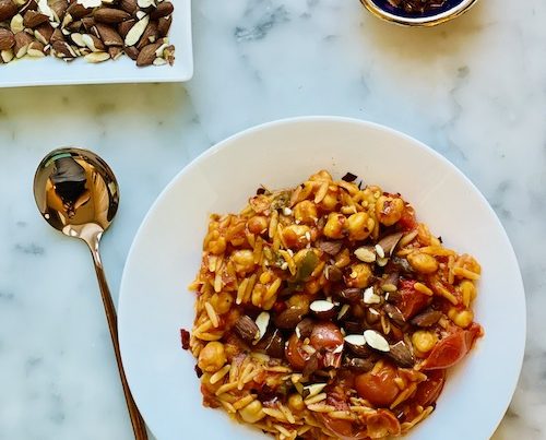 Mediterranean orzo stew in a white bowl with a gold spoon.