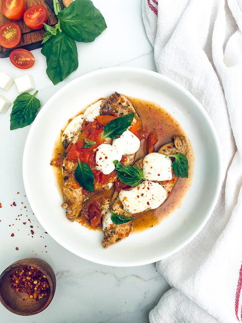 A white bowl filled with caprese chicken.