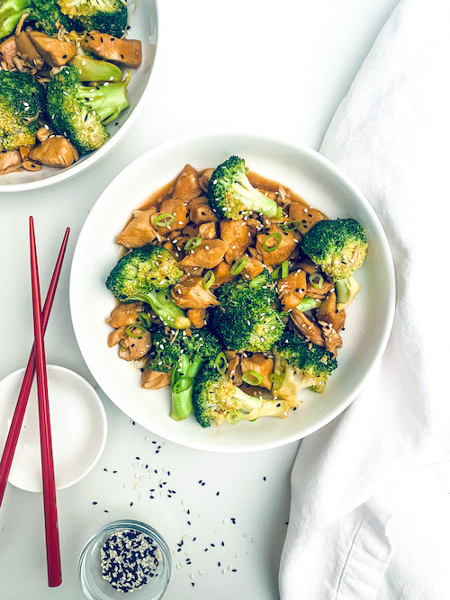 Chicken teriyaki with broccoli in a white bowl with chopsticks.