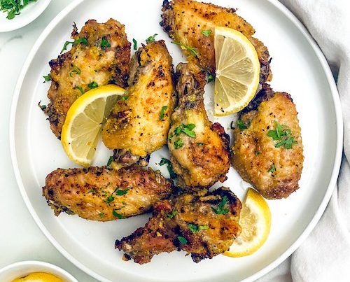 Crispy fried lemon pepper chicken wings with lemon wedges on a plate.