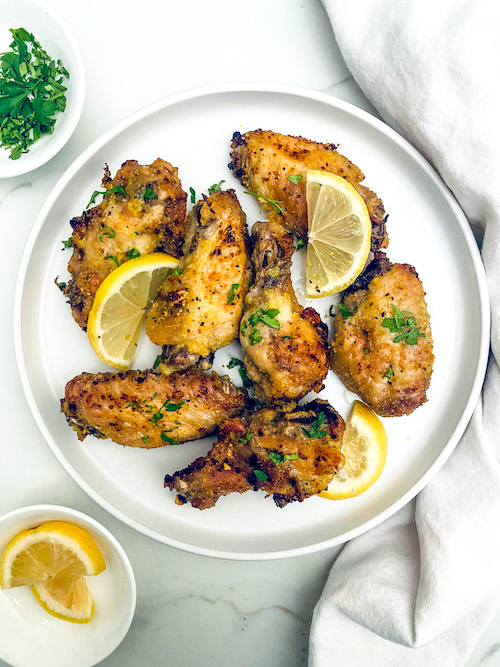 Crispy fried lemon pepper chicken wings with lemon wedges on a plate.