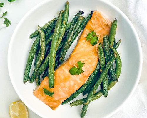 Honey mustard glazed salmon and green beans on a white dinner plate.