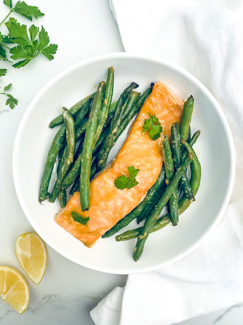 Honey mustard glazed salmon and green beans on a white dinner plate.