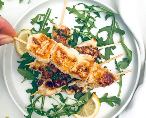 Grilled chicken kebabs on a bed of arugula and lemon slices.