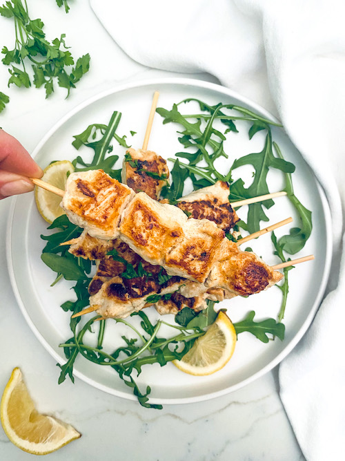 Grilled chicken kebabs on a bed of arugula and lemon slices.