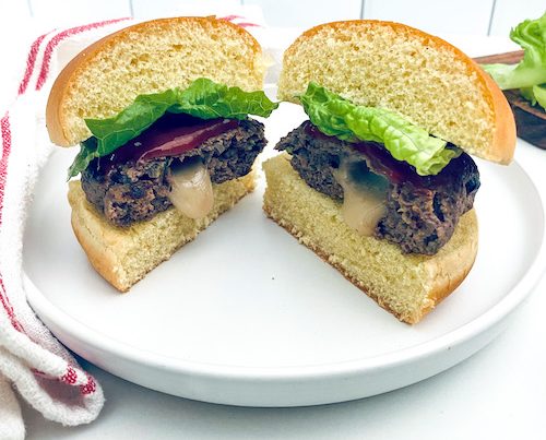 A juicy Lucy burger cut in half on a bun with lettuce.